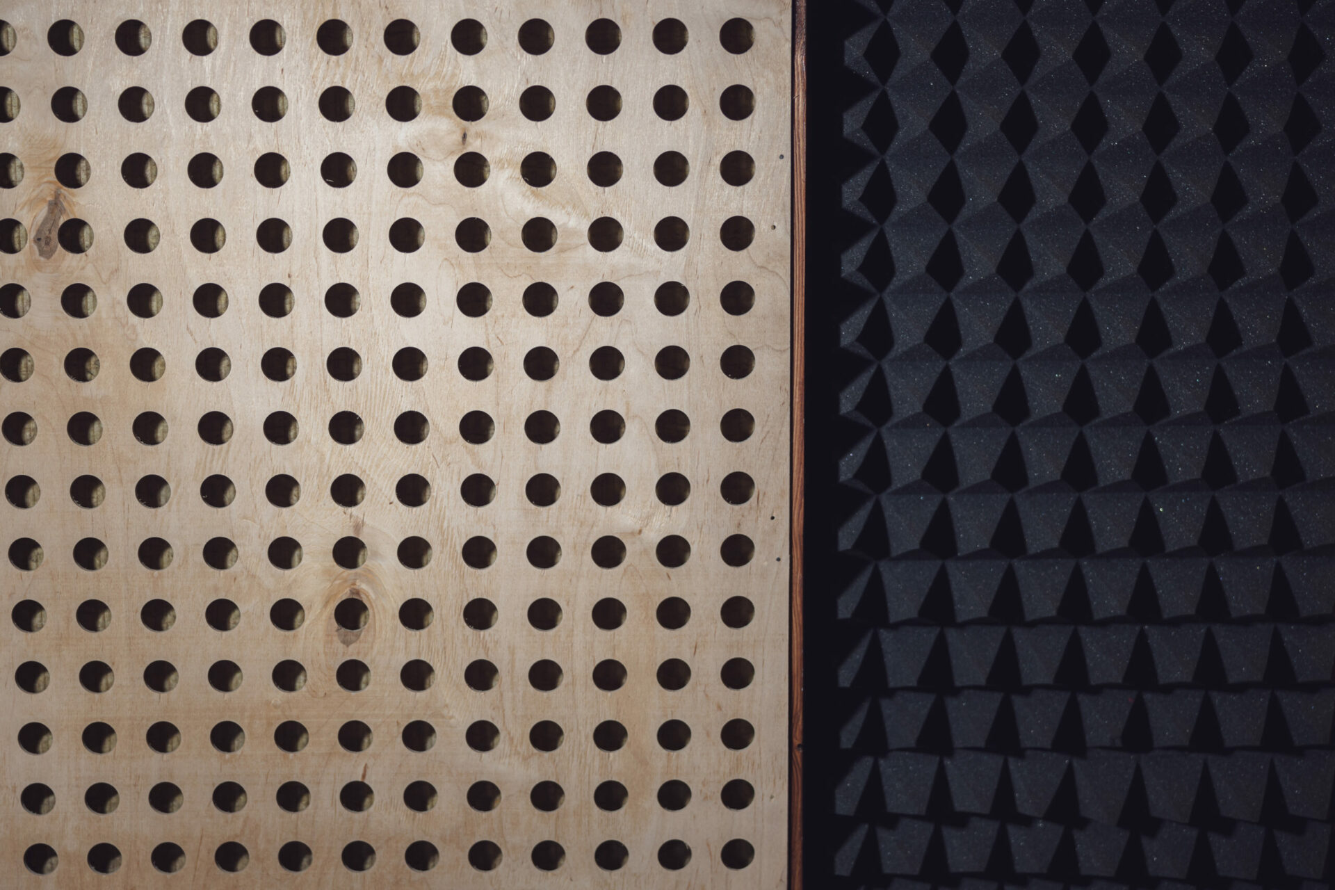 Wooden surface with round holes and black soundproof wall with acoustic dampening foam. Texture, pattern, background. Close-up of sound proof coverage in music sound recording studio.